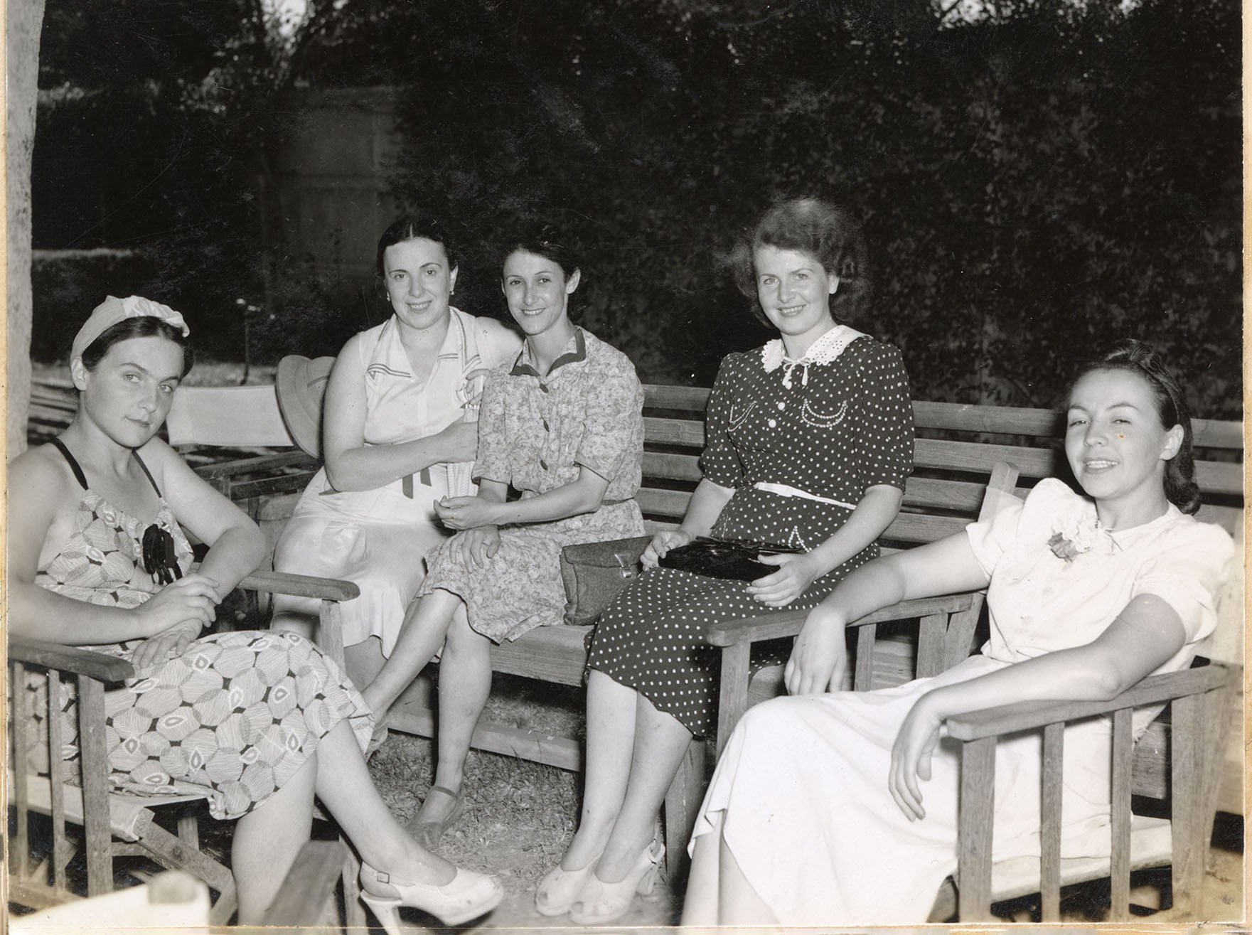 Five women sit outdoors on chairs and a bench